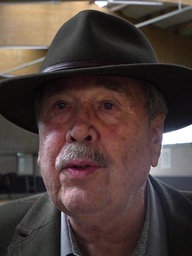 Anton van den Boom, ein älterer Mann mit Hut, steht in einer Reithalle.