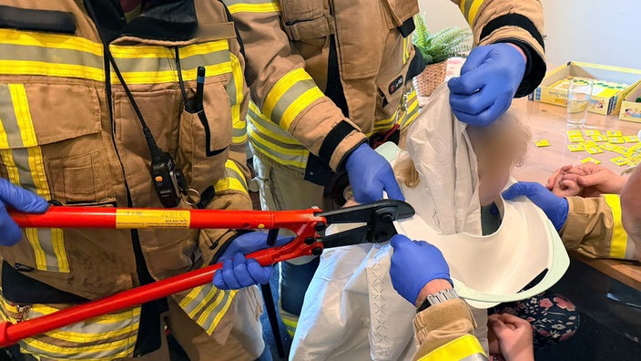 Ein Kind steckt mit dem Kopf in einem Toilettensitz. Einsatzkräfte versuchen es mit Werkzeug zu befreien.