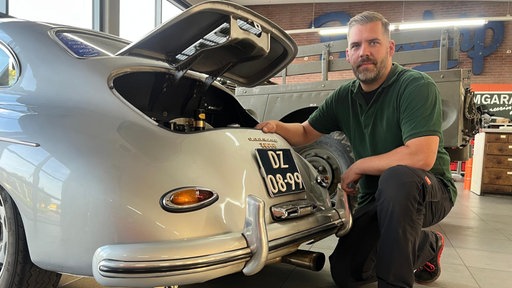 Ein Mann kniet vor dem Heck eines alten Porsches