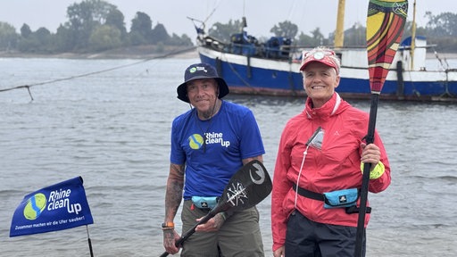 Uwe Franken und Judith Mörschel mit ihren Stand-up-Paddle-Boards vor einem Boot auf dem Rhein