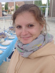 Eine Frau steht draußen vor einem gedeckten Tisch und lächelt in die Kamera
