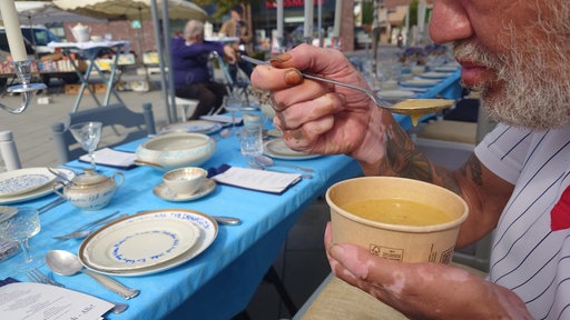 Ein Mann mit dreckigen Händen isst Suppe aus einer Pappschüssel