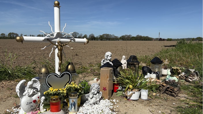 Ein weißes Kreuz und diverse Kerzen, Steine und Blumen, die an Verkehrstote erinnern sollen
