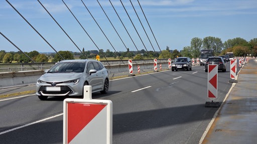 Autos fahren auf einer Brücke. Darauf stehen Baustellenschilder. 