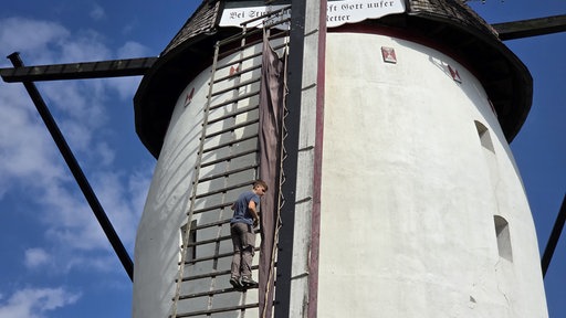 Lars Spickermann klettert den Flügel der Windmühle hoch und spannt das Segel