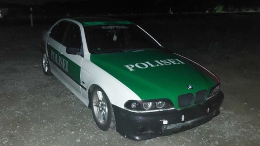 Ein Auto in dem grün-weiß älterer Polizeiautos mit der Aufschrift "Polisei".