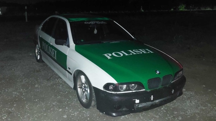 Ein Auto in dem grün-weiß älterer Polizeiautos mit der Aufschrift "Polisei".