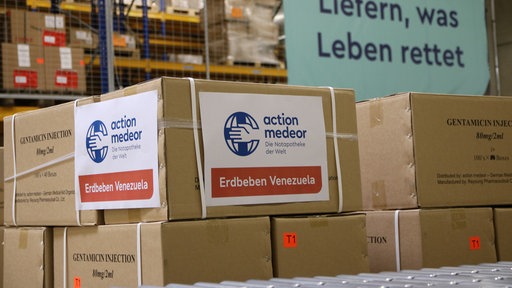 Kartons mit einem Zettel "Action Medeor" und "Erdbeben Venezuela" stehen fertig gepackt in einer Halle.