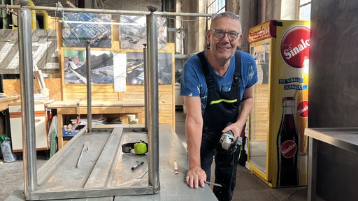 Thomas Goyke steht mit Arbeitskleidung und Flex an einem Tisch