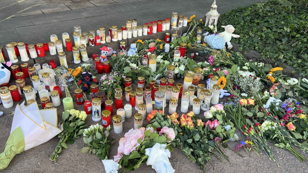Auf einem Straßenstück liegen zahlreiche Blumen, Grabkerzen und Stofftiere 