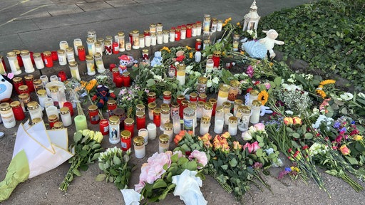 Auf einem Straßenstück liegen zahlreiche Blumen, Grabkerzen und Stofftiere 