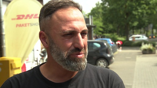 Ein Mann mit dunklen Haaren und Bart schaut seitlich an der Kamera vorbei