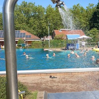 Viele Menschen sind im Schwimmbecken. Eine Dusche sprüht Wasser.