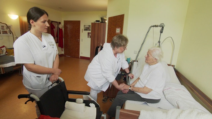 Zwei Pflegerinnen vor dem Bett einer Seniorin