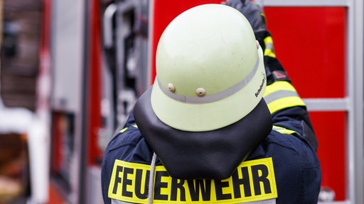 Ein Feuerwehrmann von hinten mit Kluft und Helm an einem Feurerwehrauto