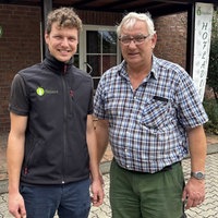 Julius Heinen und Peter Heinen stehen nebeneinander vor einem Haus und lächeln in die Kamera.