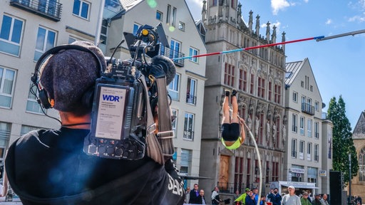 Ein Mann beim Stabhochsprung der von einem Kameramann des WDR gefilmt wird