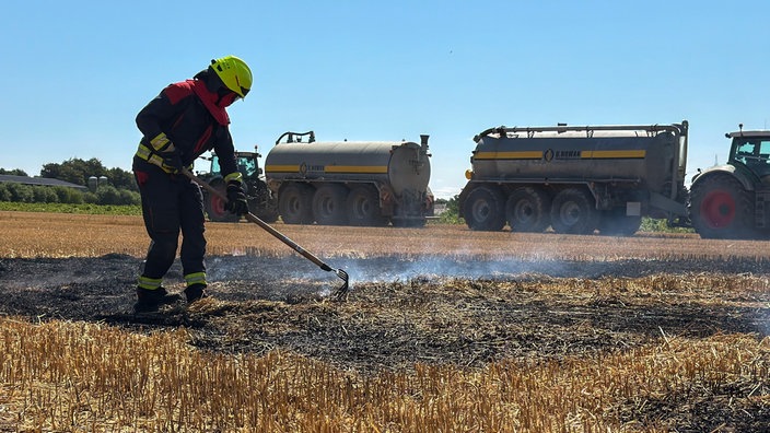 Ein Feuerwehrmann kontrolliert nach einem Brand auf einem Feld, ob alles gelöscht ist