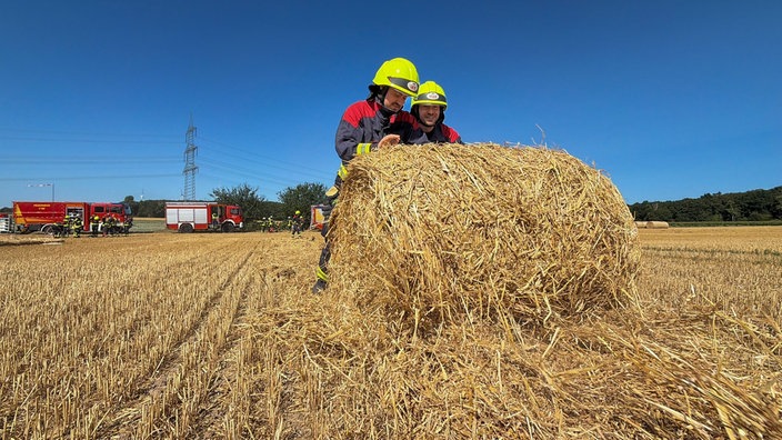 Zwei Feuerwehrmänner rollen einen Strohballen aus