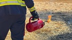 Ein Feuerwehrmann hält einen Behälter mit Flamme in der Hand
