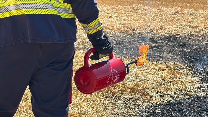 Ein Feuerwehrmann hält einen Behälter mit Flamme in der Hand
