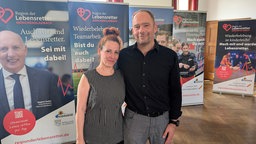 Zwei Menschen stehen vor Bannern mit der Aufschrift "Region der Lebensretter Mönchengladbach"