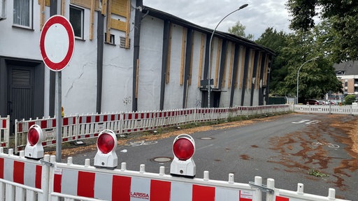 Eine Straße die weiträumig mit Baustellenbarken abgesperrt ist. Im Hintergrund ist das marode und einsturzgefährdete Kino zu sehen.