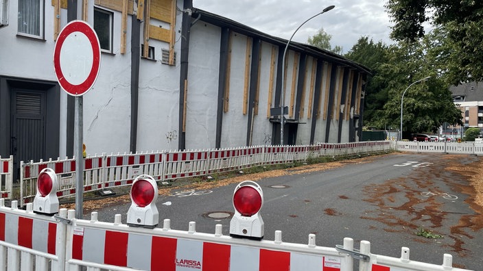 Eine Straße die weiträumig mit Baustellenbarken abgesperrt ist. Im Hintergrund ist das marode und einsturzgefährdete Kino zu sehen.