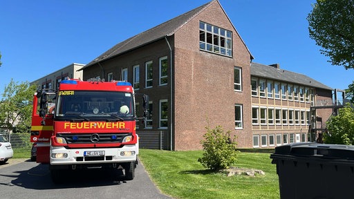 Ein braunes Schulgebäude, davor steht ein großer Feuerwehrwagen.
