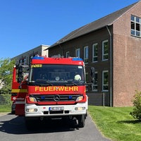 Ein braunes Schulgebäude, davor steht ein großer Feuerwehrwagen.