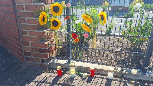 Vor einem Industriegelände stehen Blumen und Kerzen