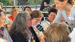 Eine Moderatorin hält ein Mikro und eine Zuschauerin im Publikum spricht