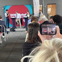 Eine Zuschauer macht ein Handyfoto, im Hintergrund ein Podium mit drei Gästen und einem Moderator
