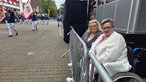 Zwei Frauen sitzen hinter einer Absperrung und schauen sich die marschierenden Schützen an. 