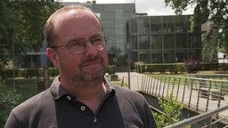Ein Mann mittleren Alters mit Brille steht draußen und schaut in die Kamera.