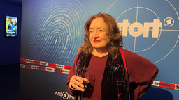 Wilhelmine Klemm posiert vor Tatort-Fotowand mit Sektglas