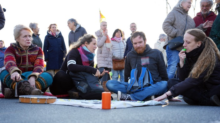 Menschen sitzen mit einem Banner und trillerpfeifend auf einer Straße