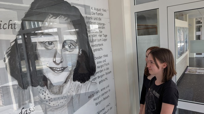 Zwei Schülerinnen betrachten eine Informationstafel zum Leben von Anne Frank.