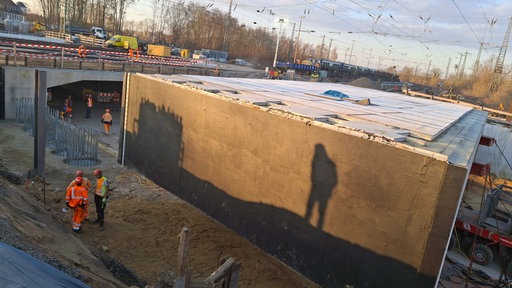 Baustellenauschnitt bei Herford, wo eine Brücke am Bahnhof gebaut werden soll. Ein paar Baustellenarbeiter laufen herum.