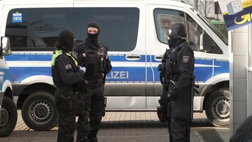 Vier vermumte Polizeibeambte vor einem Polizeibus.