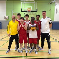 Fünf junge Basketballspieler stehen mit zwei Trainern vor einem Basketballkorb