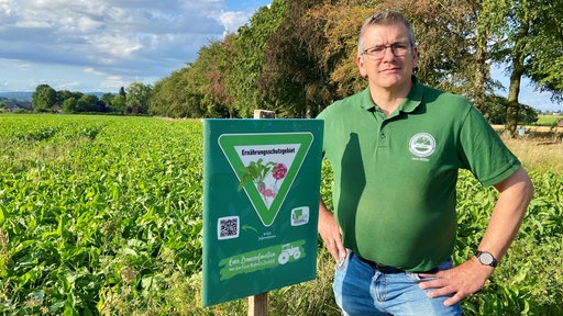 Jens Müller steht im Feld vor einem der Schilder mit der Aufschrift "Ernährungsschutzgebiet"