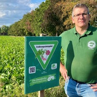 Jens Müller steht im Feld vor einem der Schilder mit der Aufschrift "Ernährungsschutzgebiet"