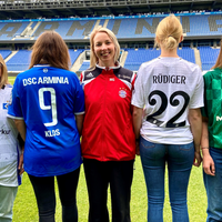Fünf Frauen im Stadion, die Fußballtrikots tragen.