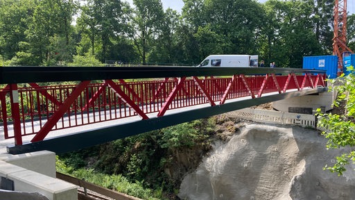 Auf dem Foto ist eine rot-schwarze Brücke aus Aluminium über den Biggesee.