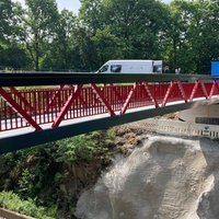Auf dem Foto ist eine rot-schwarze Brücke aus Aluminium über den Biggesee.