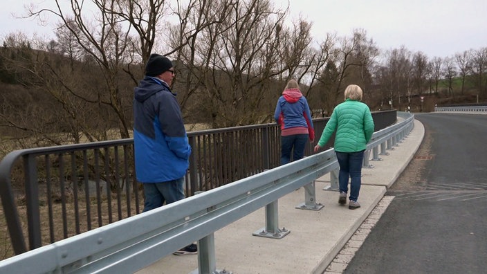 Drei fußgänger laufen auf dem schmalen Fußweg links und rechts der Leitplanke 