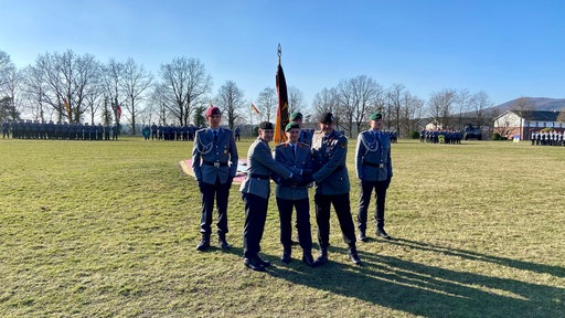 Fahnenübergabe: Fünf Soldaten stehen auf einer Wiese um eine Fahne herum.
