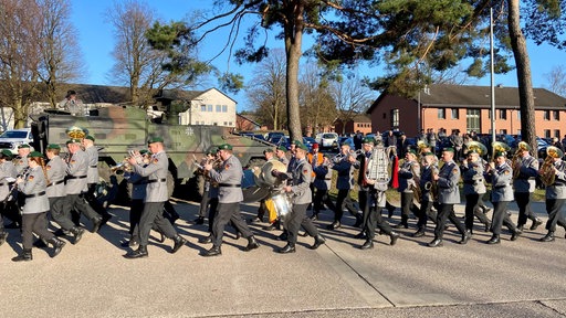 In Uniform gekleidete Menschen marschieren, dabei spielen sie verschiedene Instrumente.