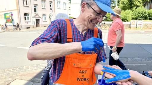 Klaus Selinger malt Hände blau.